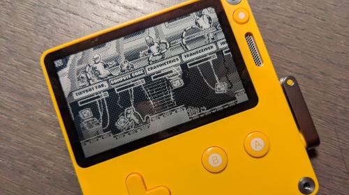 A photo of a PlayDate handheld console, running a early build of the Widget Satchel spin-off game that Mark is developing for it.