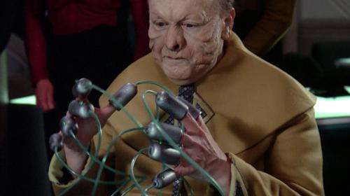 A screenshot from the Star Trek episode "Peak Performance," showing the character Kolrami with wired attachments on each of his 10 fingers, playing the fictional video game "Strategema."