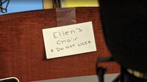 A close-up photo of a char with a taped-on sign that says "Ellen's Chair *DO NOT LICK*."