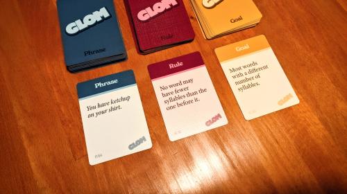 Three decks from the tabletop game "GLOM," with one card dealt from each deck.