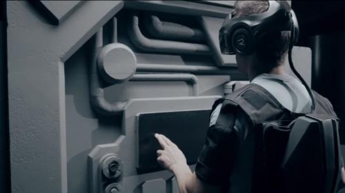 A photo of a man wearing a VR headset and portable computer vest, interacting with a physical setpice.