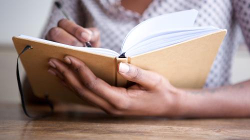 A woman writes by hand in a paper journal.