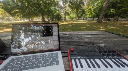 A point-of-view photo of a laptop and MIDI keyboard set up on a picnic table at Queen's Park in Toronto.