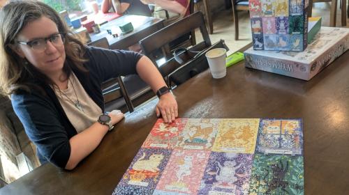 A photo of Ellen admiring a completed 500-piece jigsaw puzzle. The puzzle's image is a grid of 12 illustrations of a cats, each representing a different zodiac sign.