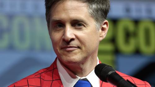 A photo of Yuri Lowenthal. He is wearing a red suit jacket with black grid lines, and a blue tie.