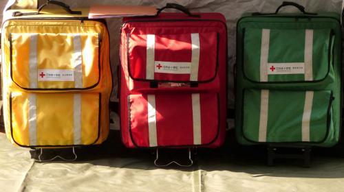 A photo of three color-coded medical kit bags (yellow, red, green) sitting on the ground.