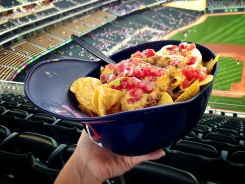 Photo of a large helping of cheesy nachos in a bowl styled like an upside-down baseball helmet.