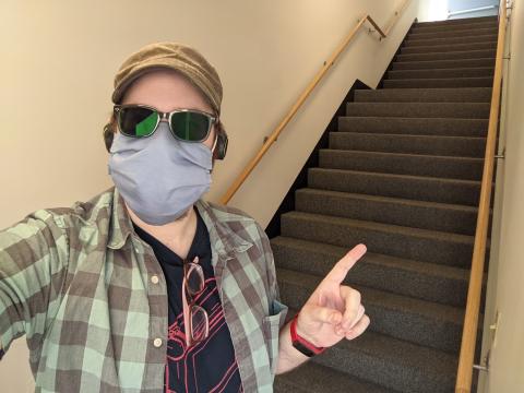 A selfie of Mark, wearing sunglasses and a cloth face mask, at the bottom of a staircase, pointing up.