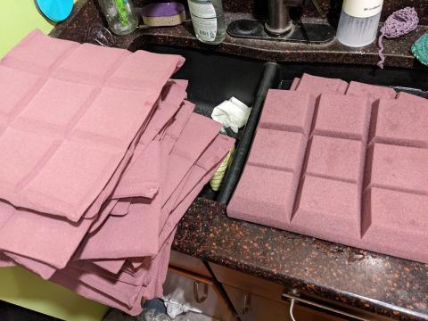 A photo of a stack of vacuum-compressed acoustic panels next to a kitchen sick where two of the panels are submerged in water.