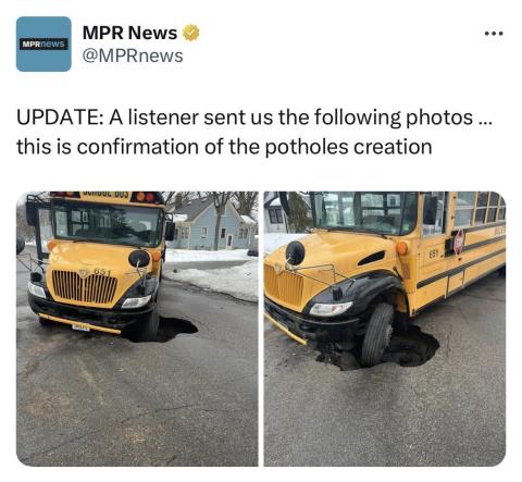 A terrifying sinkhole in the middle of a city street, presumably revealed by a school bus driving over it. The front tire of the school bus is stuck in the sinkhole.