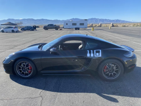 A photo of Kris's sportscar. It's a sleek black car with 110 in white font on the side. Apologies, the writer does not know the model of the car. In the background is a vast parking lot in a desert framed by mountains.